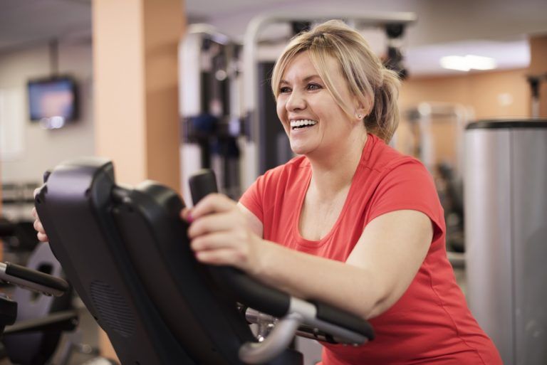 happy woman riding on exercise bike at the gym ZHEQX3N 1 768x513