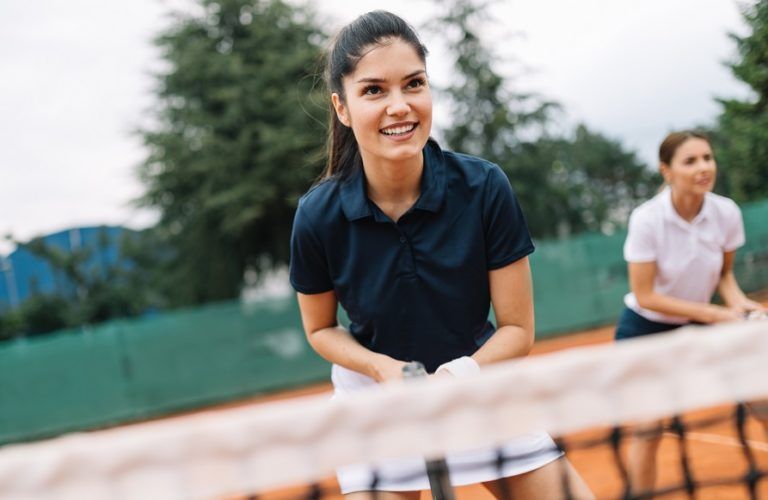 young happy women friends playing tennis at tennis RQL2MU8 768x500